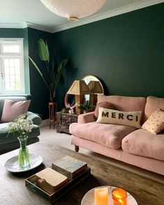 a living room with green walls and pink couches, coffee table and mirror on the wall