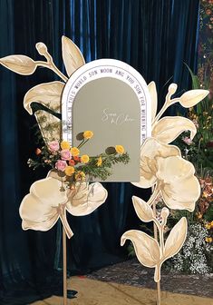 a mirror with flowers on it in front of a blue curtained background and a sign that says, i love you to the moon