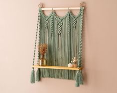 a wall hanging with some tassels on it and a vase filled with flowers