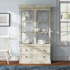 a white china cabinet sitting in a living room next to a chair and table with plates on it