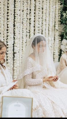 two women in wedding gowns sitting next to each other and one woman wearing a veil