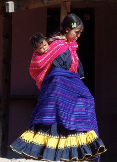 two women in colorful dresses walking down the street with one carrying a child on her back