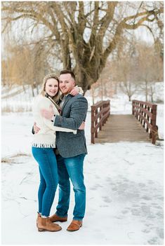 a man and woman hugging in the snow by a wooden bridge during their winter engagement session