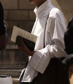 a woman in white shirt and black pants holding a book