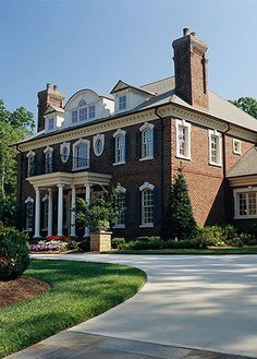 a large brick house with white trim and columns on the front, surrounded by greenery