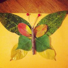 a butterfly made out of leaves sitting on top of a wooden table next to a yellow wall