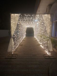 a tunnel with lights on the sides and white curtains over it, in front of a building