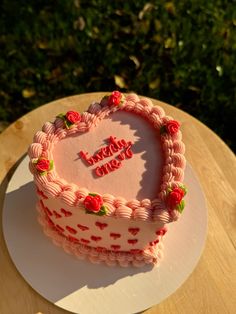 a heart shaped cake sitting on top of a wooden table next to a green bush