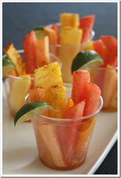 small cups filled with watermelon and pineapple slices on a white platter