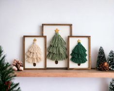 three framed christmas trees on a mantle with pine cones