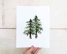 a person holding up a card with watercolor trees on it