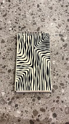 a black and white zebra print notebook sitting on top of a stone floor next to pebbles