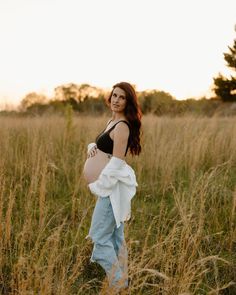 a pregnant woman is standing in the tall grass