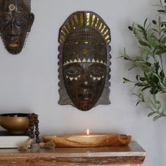 two african masks hanging on the wall above a table with a candle in front of it