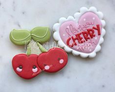 two decorated cookies sitting next to each other on top of a white table with the words i love you cherry