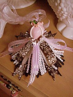 a pink and brown brooch sitting on top of a wooden table next to white vases