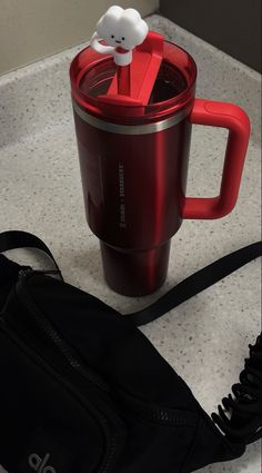 a red coffee cup sitting on top of a counter next to a black bag and purse