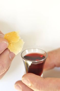 a person holding a piece of bread next to a small cup filled with red liquid