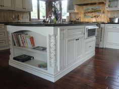 a kitchen with white cabinets and black counter tops, an island in the middle has books on it