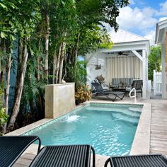 an outdoor swimming pool with lounge chairs around it and trees surrounding the pool area in front of the house