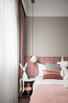 a pink bed with two stuffed animals on the headboard and pillows in front of it