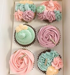 six cupcakes in a box decorated with pastel frosting