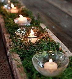 candles are lit in glass bowls with moss growing on the sides, along with small rocks and wood planks