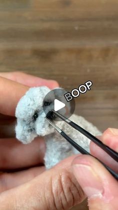 someone is crocheting a small white teddy bear with black yarn and scissors in their hands