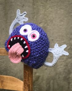 a crocheted hat with an open mouth and large teeth on top of a wooden chair