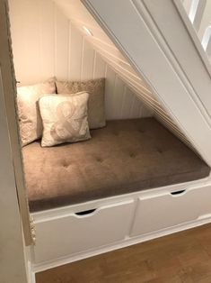 a window seat in the corner of a room with two pillows on top of it