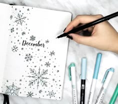 a person writing on a notebook with pens and markers next to it, surrounded by snowflakes