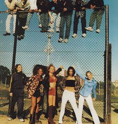 a group of young people hanging from a chain link fence with their arms in the air