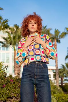 a woman with red hair is standing in front of some palm trees and wearing jeans