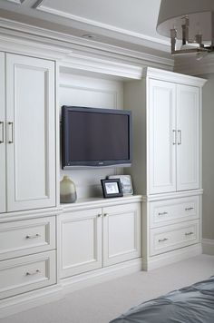 a flat screen tv mounted to the side of a white wall in a bedroom with built - in cabinets