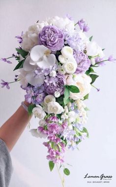 a bride's bouquet with purple and white flowers on the bottom is held by her hand