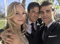 two men and a woman are posing for a picture in front of a tree with their arms around each other