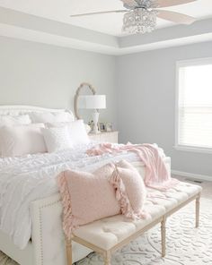 a bedroom with a large bed and two windows in the corner, along with white furniture