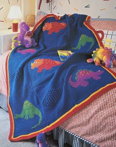 a crocheted dinosaur blanket on top of a bed next to a stuffed animal