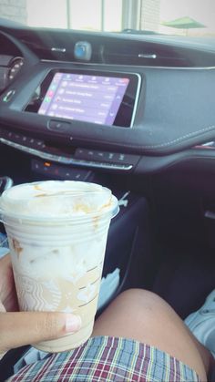 a person holding up a cup of coffee in front of a car dashboard with the screen on