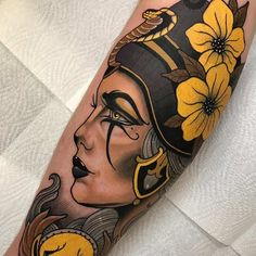 a woman's face with flowers in her hair and an egyptian mask on her arm