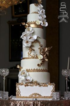 a three tiered wedding cake with white and gold flowers on the top, sitting on a table