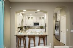 a kitchen with two bar stools in front of the counter and an archway leading to the living room