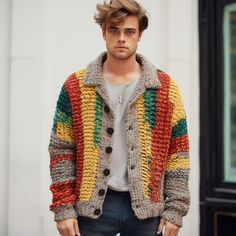 a young man wearing a multicolored knitted jacket and jeans standing in front of a building