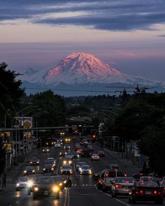 a city street filled with lots of traffic under a snow covered mountain in the distance