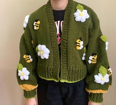 a young boy wearing a green knitted jacket with flowers and bees on the sleeves