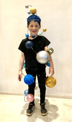 a young boy dressed up as an alien with planets on his head and hands, standing in front of a white wall