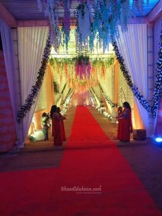 a red carpeted aisle with white drapes and flowers hanging from it's ceiling