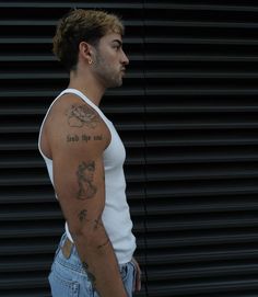 a man with a tattoo on his arm standing in front of a black metal wall