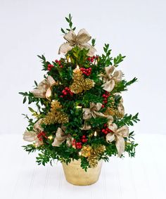 a potted christmas tree decorated with gold and red berries, pine cones and bows