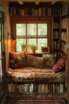 a living room filled with lots of books next to a window covered in pillows and blankets